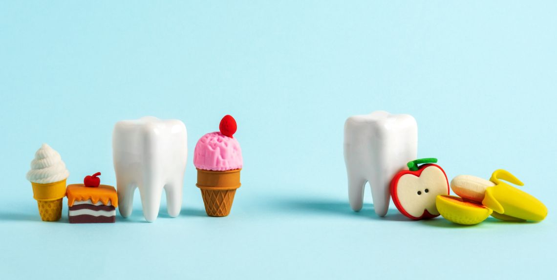 Modelo de dientes con alimentos dulces y frutas que representan el impacto positivo y negativo de la dieta en la salud dental